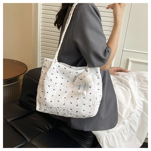 Detail of white quilted tote bag featuring black bow embroidery and plush cloud charm