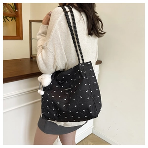 Close-up of black tote bag with white bow print, woven strap, and cloud charm detail