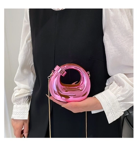 Detail of metallic pink swipe bag with gold chain strap on a white shirt background