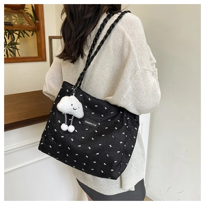 Detail of black tote bag with white bow prints and a plush cloud charm on a woven strap