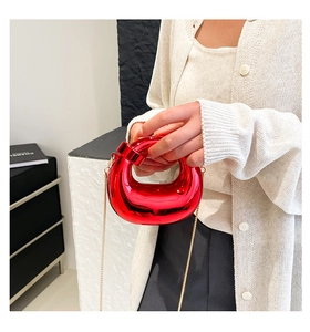 Detail of red crescent bag with glossy mirror finish and gold chain strap held by model