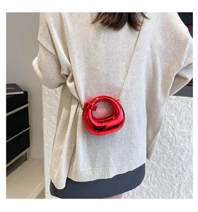 Close-up of a mini red metallic crescent bag with chain, shown on a beige knit sweater