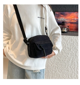 Detailed close-up of black corduroy crossbody bag with woven zipper pull and adjustable strap
