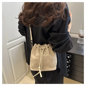 Detail of light beige drawstring bucket bag featuring golden hardware and leather strap