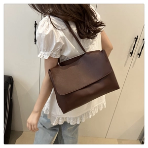 Side view of a deep brown leather tote bag worn by a model in a minimalist home setting