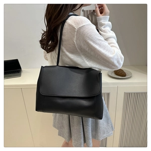 Close-up of black minimalist leather shoulder bag worn by model in a modern daily setting