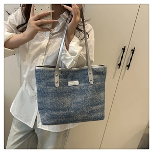 Close-up of denim blue tote bag showing washed texture and silver metal logo plaque