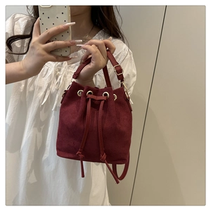 Macro shot of a red suede bucket bag with a drawstring closure and gold hardware