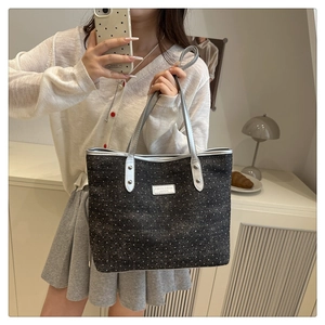Detail of grey polka dot tote bag with silver handles and metal logo plate