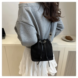 Detail of a black canvas drawstring bucket bag worn by a model in a clean indoor setting