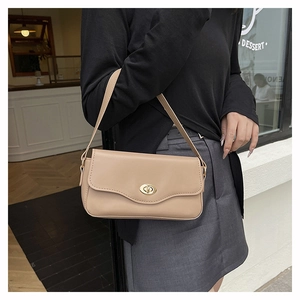 Detail of a beige leather crossbody bag with a gold oval turn-lock on a stylish model