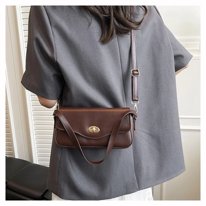 Detail view of dark brown leather baguette bag worn over shoulder with a gray blazer