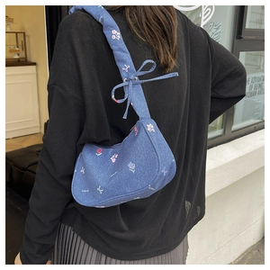 Détail de la broderie fleurie et des nœuds sur le sac hobo en jean porté à l'épaule