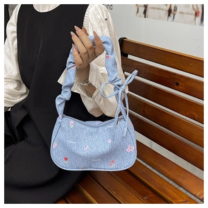 Détail du petit sac floral en denim bleu avec anse froncée et décoration de ruban