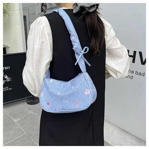 Sac sous le bras en denim bleu à imprimé fleuri avec nœud porté par un mannequin