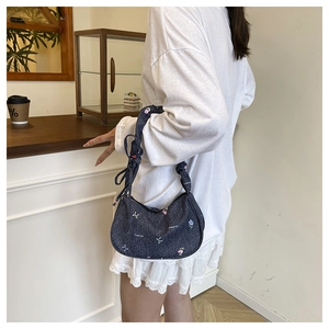 Détail du sac d'épaule en denim bleu foncé avec broderies de fleurs et motifs de nœuds