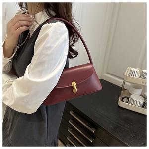 Detail of burgundy leather underarm bag featuring an elegant gold oval metal clasp closure