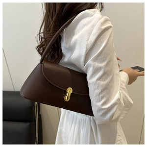 Detailed view of deep coffee baguette bag with golden oval buckle worn as shoulder bag