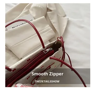 Detail shot of smooth silver metal zipper and red interior lining on a white handbag