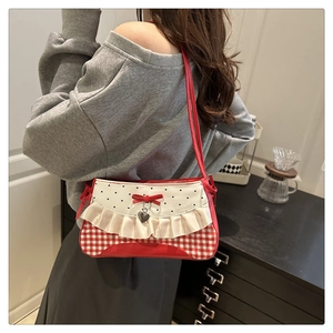 Detail of red gingham shoulder bag with cream ruffles and silver heart charm on model