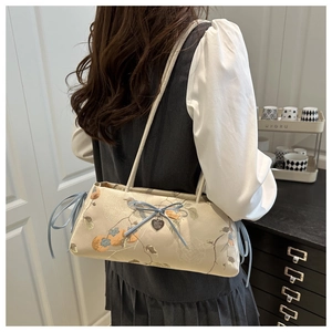 Detail of a chic bow and heart charm on a floral jacquard underarm tote bag