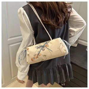 Detail of embroidered tote bag with blue bows and heart pendant shown on shoulder