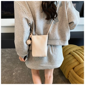 Back view of a model wearing a beige lychee leather mini crossbody phone bag with charm