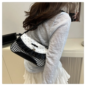 Detail of lace ruffles and heart pendant on a checkered baguette shoulder bag