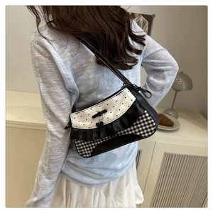 Close-up of checkered underarm bag with ruffled edges and heart pendant on shoulder