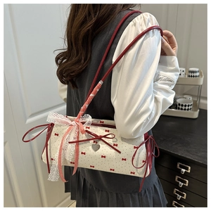 Detail of white tote bag with red bow print, lace trim and heart charm on a shoulder strap