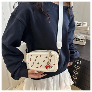 Detail of crossbody bag featuring red cherry prints and decorative 3D cherry pendant