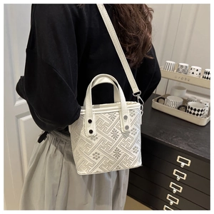 Detail view of a white textured crossbody bag with grey geometric patterns on a model