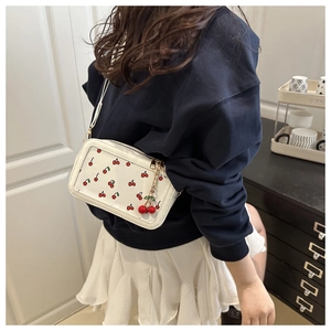 Detail view of white crossbody bag with red cherry prints and decorative cherry charm
