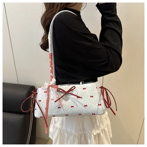 Detail of red bow prints and heart metal pendant on a white lace-trimmed tote bag
