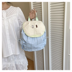 Close-up of a cute light blue nylon backpack with a pear-shaped cream flap and green piping