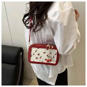Detail of red cherry pattern on white canvas bag with leather strap and cherry charm