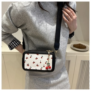 Detail of a white crossbody camera bag with red cherry prints and dual zip compartments