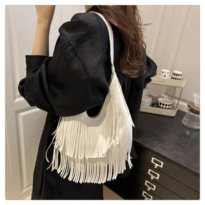 Detalle de bolso hobo blanco con flecos de cuero sobre ropa de lino color negro