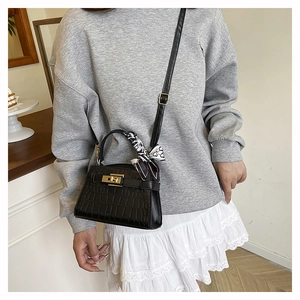 Detail of black crocodile pattern handbag with gold clasp and geometric silk scarf handle