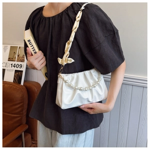 Detail of white pleated cloud bag with pearl chain and satin strap shown on a model