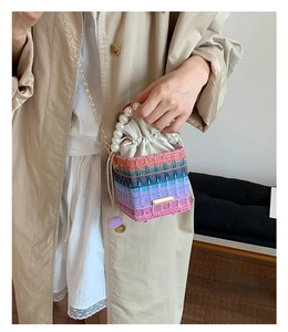Detail of colorful woven bucket bag with pearl handle and golden chain strap