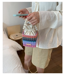 Close-up of colorful woven bucket bag with pearl handle and metallic chain strap