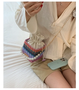 Detail of colorful woven bucket bag featuring large pearl handle and gold chain strap