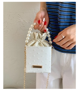 Detail of white textured mini bucket bag with pearl handle and golden chain strap