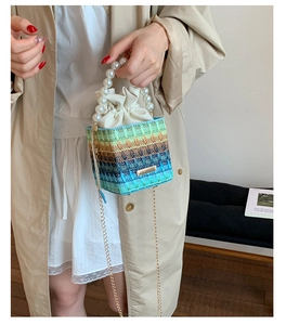 Detail of colorful woven bucket bag featuring pearl handle and gold chain strap