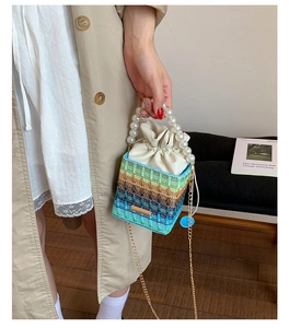 Detail of gradient woven bucket bag featuring large pearl handle and gold chain strap