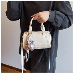 Detail view of white Boston bag featuring 3D bear embossing and plush charm accessory