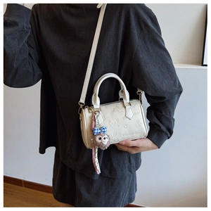 Detail of cream-white Boston bag featuring embossed cartoon bears and plush monkey charm