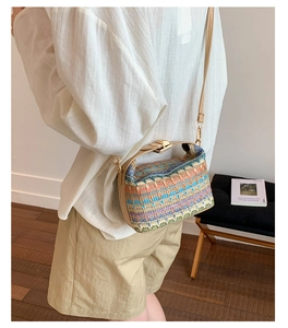 Detail of colorful woven straw bucket bag with brown leather strap and gold hardware