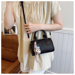 Detail of black embossed leather handbag featuring cartoon patterns and plush charm